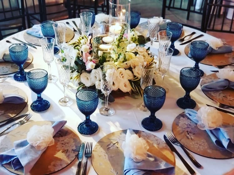 Mesa posta com taças azuis e flores brancas